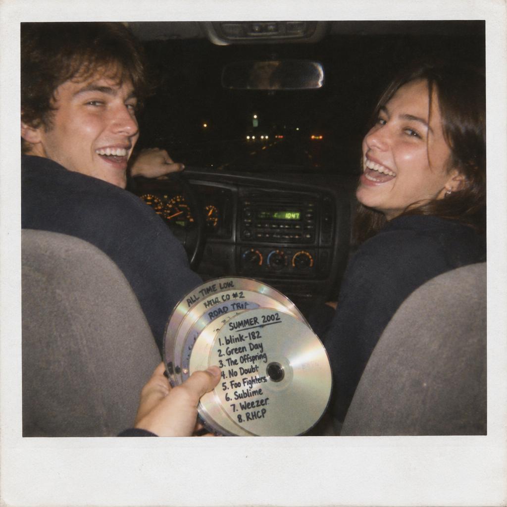Two friends in a car at night holding a fan of burned CDs